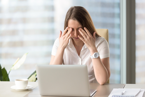 women sitting at desk rubbing eyes 