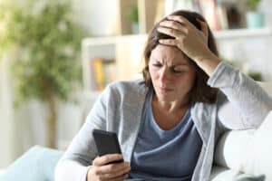 Woman holding her head and looking at her phone