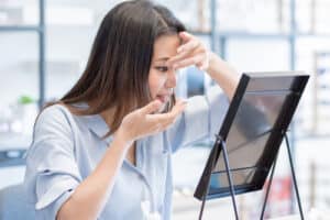 woman using mirror to put contact lenses into her eyes 