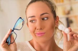 woman holding eyeglasses and pack of contact lenses 